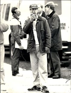 black and white photograph of a man standing on the sidewalk with his hands in his mouth