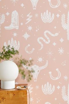 a white vase sitting on top of a wooden table next to a wall with cactus designs