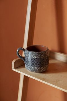 a blue and white cup sitting on top of a wooden shelf next to an orange wall