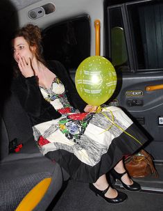 a woman sitting in the back seat of a car with a balloon attached to her mouth