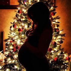 a pregnant woman standing in front of a christmas tree