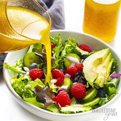 a salad with raspberries, avocado and kiwis being poured into it