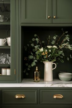 a vase with some flowers in it sitting on a kitchen counter next to green cupboards