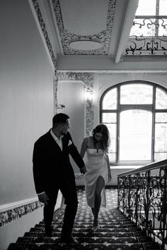 a man and woman are walking down the stairs in black and white, holding hands