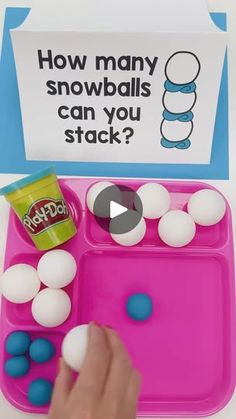 a child's hand is picking up balls from a pink tray with blue and white dots