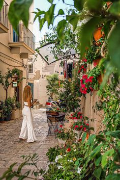 a woman in white is walking through an alleyway with potted plants on either side