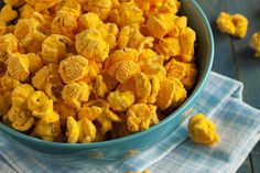 a blue bowl filled with yellow popcorn sitting on top of a wooden table next to a napkin