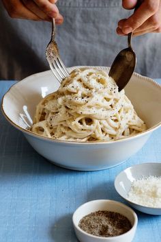 a person holding a fork and spoon over a bowl of pasta