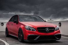 a red car parked in front of a white building with dark clouds above the cars