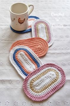 four crocheted coasters sitting on top of a table next to a coffee cup