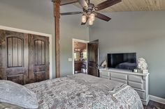 a bedroom with a bed, dresser and ceiling fan in front of a flat screen tv