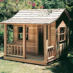 a small wooden shed with a porch and windows on the roof, in front of some trees