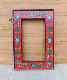 a red frame with flowers and leaves painted on the outside is sitting in front of a wooden wall