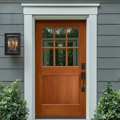 the front door to a house with two lights on it's side and bushes in front