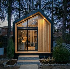 a small house with wooden siding and glass doors on the front door is lit up at night