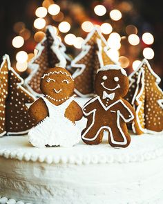 two gingerbread men standing on top of a white cake with trees in the background