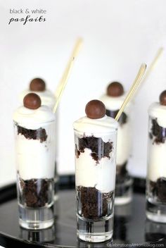 four desserts with chocolate and white frosting on a black tray in glass cups