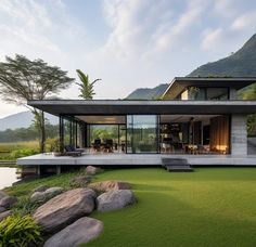 the house is surrounded by large rocks and green grass, with mountains in the background