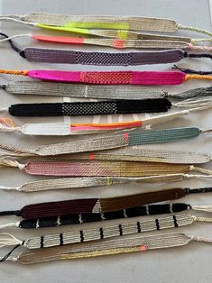 many different colored feathers are lined up on a white tablecloth with black, yellow, pink, green, and orange ribbons