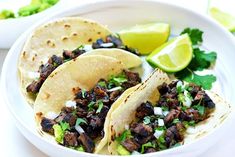 three tacos on a plate with limes and cilantro