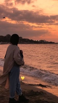 a man standing on top of a sandy beach next to the ocean at sunset or dawn