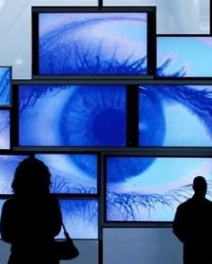 two people standing in front of multiple televisions with blue eyes on them