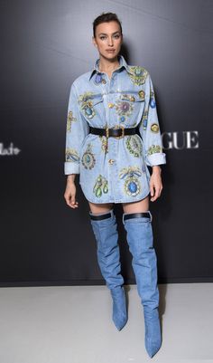 a woman standing in front of a black wall wearing thigh high boots and a denim shirt dress