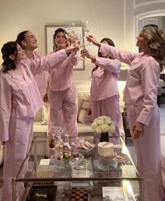 four women in pink pajamas toasting with champagne glasses on a coffee table while another woman looks on