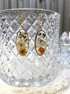 a pair of earrings sitting on top of a glass bowl next to a vase filled with flowers