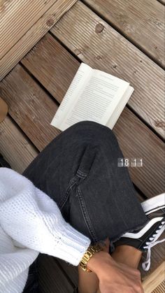 a person sitting on a wooden bench with their feet propped up and reading a book