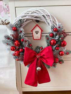 a white wreath with red ornaments and a birdhouse hanging from it's side