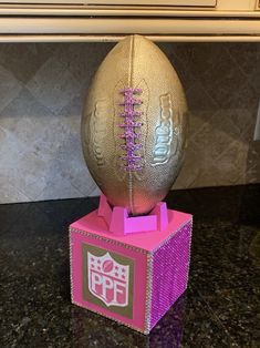 a gold and pink football sitting on top of a box with the letter p in it