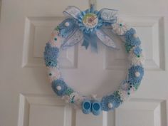 a blue and white crocheted wreath with baby shoes hanging on the front door