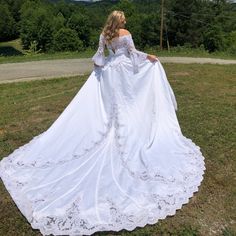 a woman in a white wedding dress standing on the grass with her back to the camera