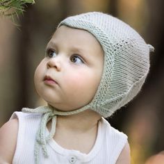 a small child wearing a knitted hat and looking up at the sky with trees in the background