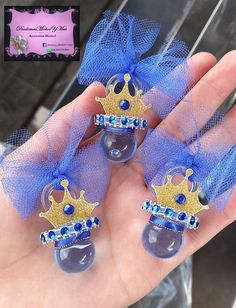 three small blue and gold crowns are held in someone's hand with a purple ribbon