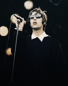 a man with sunglasses on his face holding a microphone in front of him and looking up at the sky