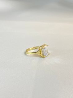 a yellow gold ring with a square cut diamond in the center on a white surface