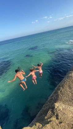 three people jumping into the ocean from a cliff