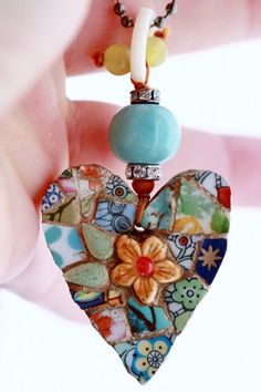 a hand holding a heart shaped pendant with flowers on it's side and beads hanging from the back