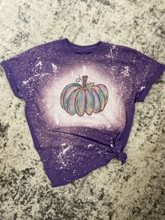 a purple t - shirt with a painted pumpkin on the front and bottom, sitting on a granite surface