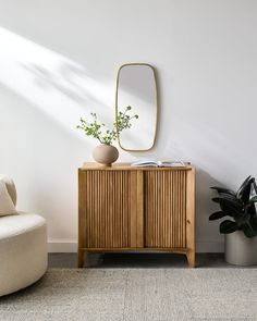 a wooden cabinet sitting next to a white chair in a room with a mirror on the wall