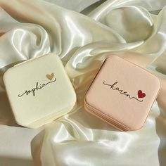 two personalized compact cases sitting on top of a white satin covered bed with the word love written in cursive writing