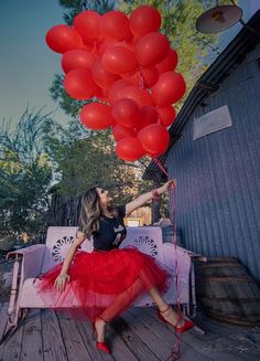 a woman is sitting on a bench with red balloons