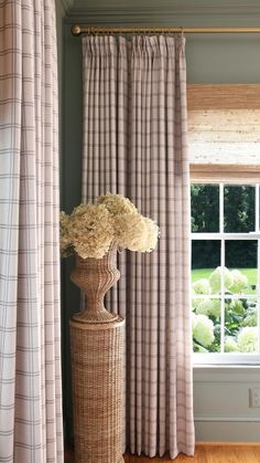 a tall vase with flowers on top of it in front of a curtained window