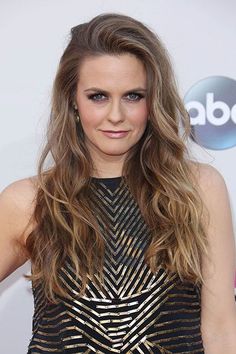 a woman with long, wavy hair wearing a black and gold dress at an event