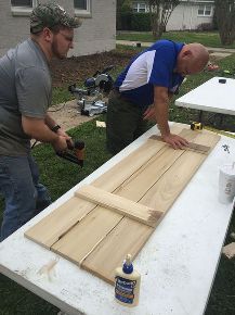 two men are working on wood planks in the yard with one man holding a drill