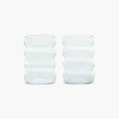 two clear vases sitting side by side on a white surface, one is empty