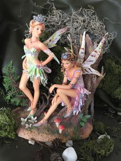 two fairy figurines sitting on top of a tree stump