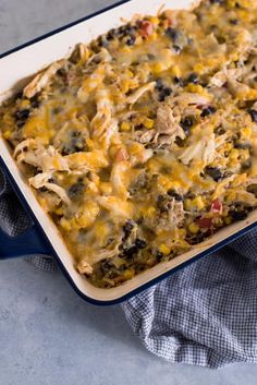 a casserole dish filled with chicken, black olives and cheese on a blue towel